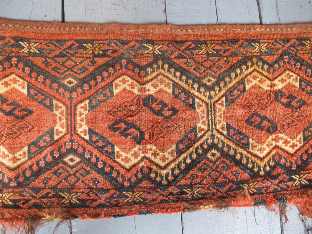A rectangular handwoven Turkmen wool bagface displaying three repeating geometric diamond medallions in red, navy, and cream with fringed bottom edges. View IV