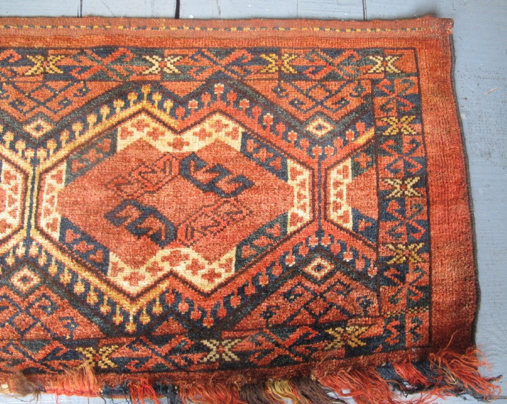 A rectangular handwoven Turkmen wool bagface displaying three repeating geometric diamond medallions in red, navy, and cream with fringed bottom edges. View V