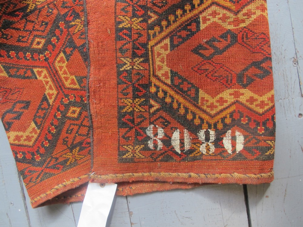 A rectangular handwoven Turkmen wool bagface displaying three repeating geometric diamond medallions in red, navy, and cream with fringed bottom edges. View X