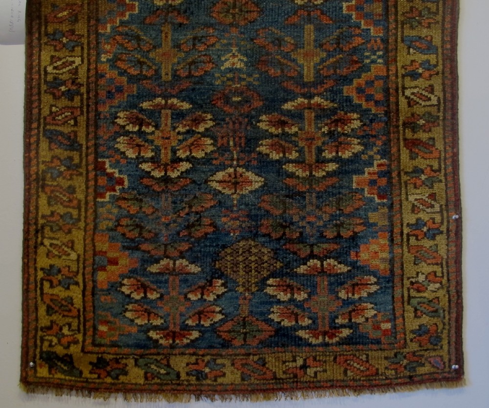 An antique hand-knotted West Persian Kurdish wool runner rug featuring repeating geometric motifs on a dark blue field framed by a patterned ochre border. View II