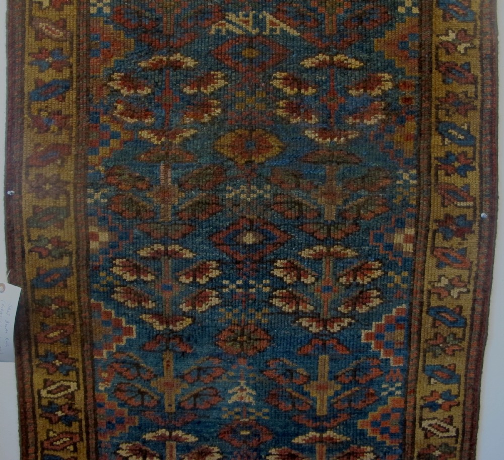An antique hand-knotted West Persian Kurdish wool runner rug featuring repeating geometric motifs on a dark blue field framed by a patterned ochre border. View III