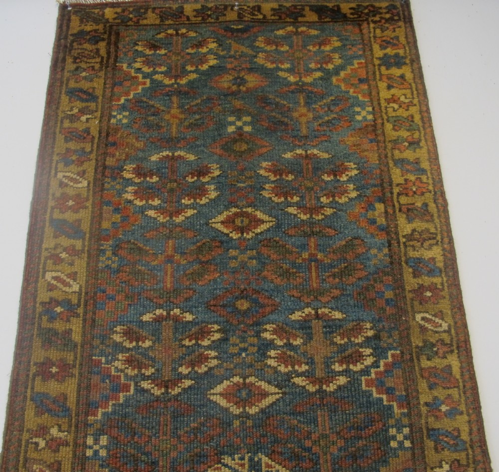 An antique hand-knotted West Persian Kurdish wool runner rug featuring repeating geometric motifs on a dark blue field framed by a patterned ochre border. View IV