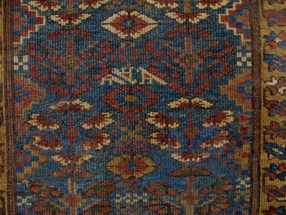 An antique hand-knotted West Persian Kurdish wool runner rug featuring repeating geometric motifs on a dark blue field framed by a patterned ochre border. View VI