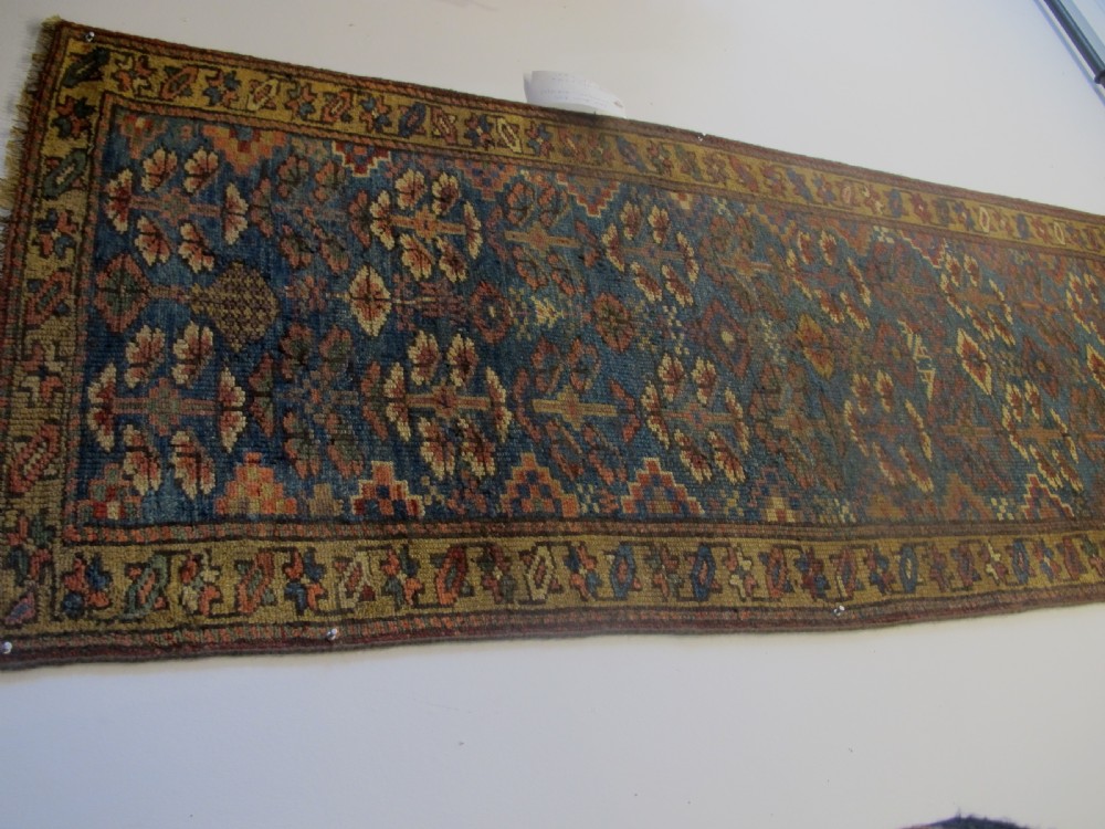 An antique hand-knotted West Persian Kurdish wool runner rug featuring repeating geometric motifs on a dark blue field framed by a patterned ochre border. View X