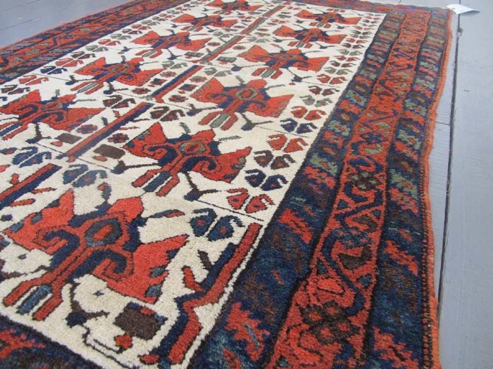 A late 19th-century Kolyai hand-knotted wool rug featuring a cream central field with stylised red and navy bird motifs framed by a geometric red border. View II