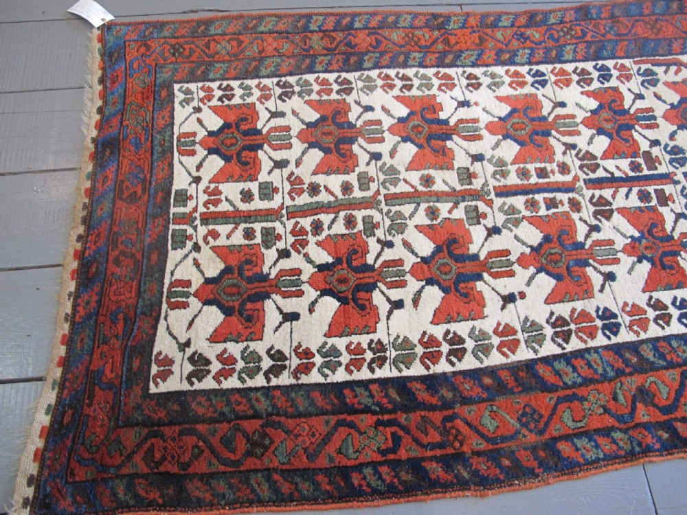 A late 19th-century Kolyai hand-knotted wool rug featuring a cream central field with stylised red and navy bird motifs framed by a geometric red border. View IV
