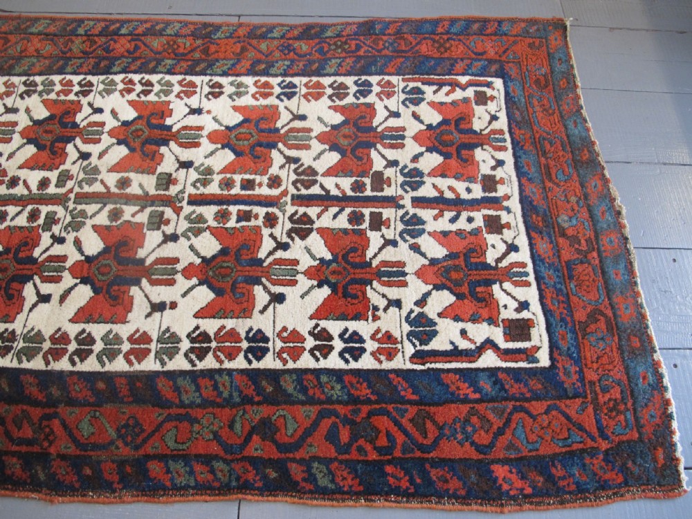 A late 19th-century Kolyai hand-knotted wool rug featuring a cream central field with stylised red and navy bird motifs framed by a geometric red border. View V