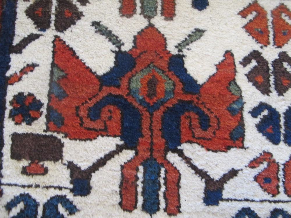 A late 19th-century Kolyai hand-knotted wool rug featuring a cream central field with stylised red and navy bird motifs framed by a geometric red border. View VI