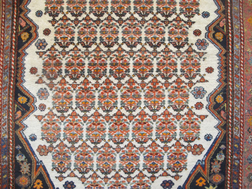 An antique hand-knotted Persian Melayir wool rug featuring an ivory central field with repeating geometric floral motifs, dark spandrels, and a terracotta border. View II