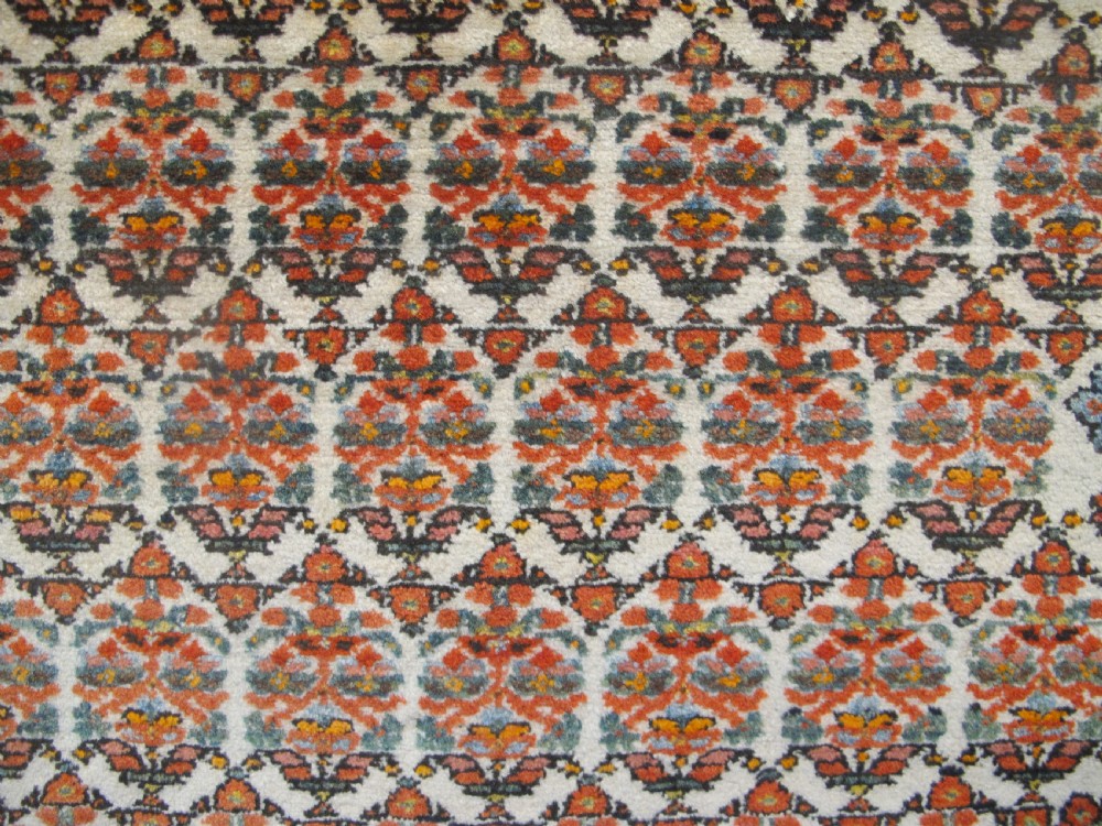 An antique hand-knotted Persian Melayir wool rug featuring an ivory central field with repeating geometric floral motifs, dark spandrels, and a terracotta border. View III