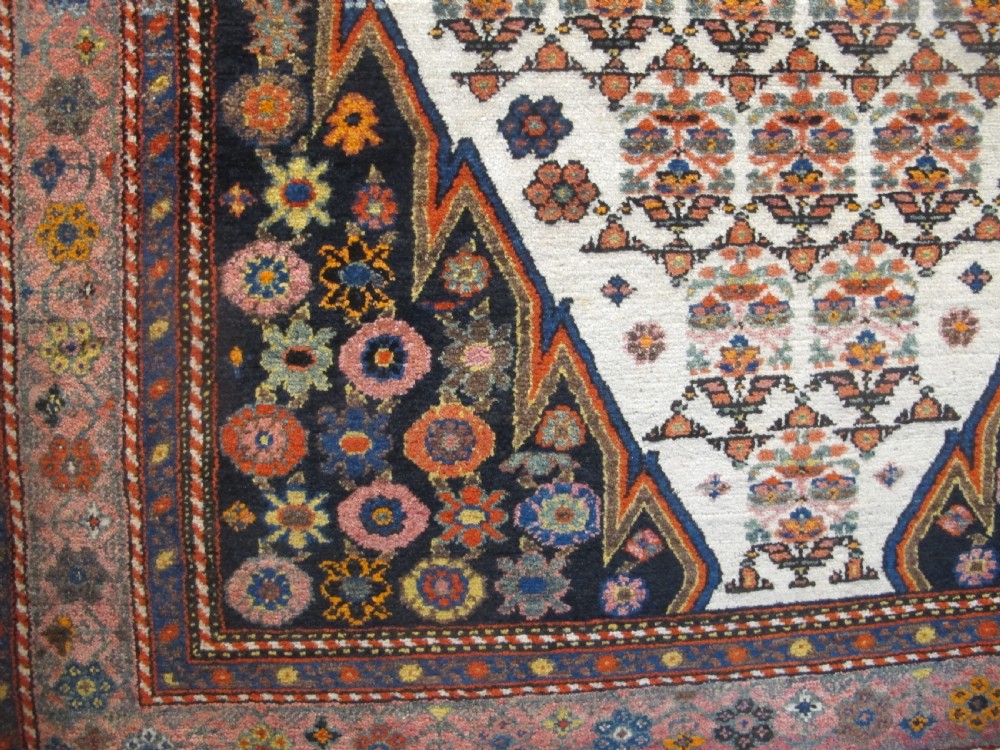 An antique hand-knotted Persian Melayir wool rug featuring an ivory central field with repeating geometric floral motifs, dark spandrels, and a terracotta border. View V