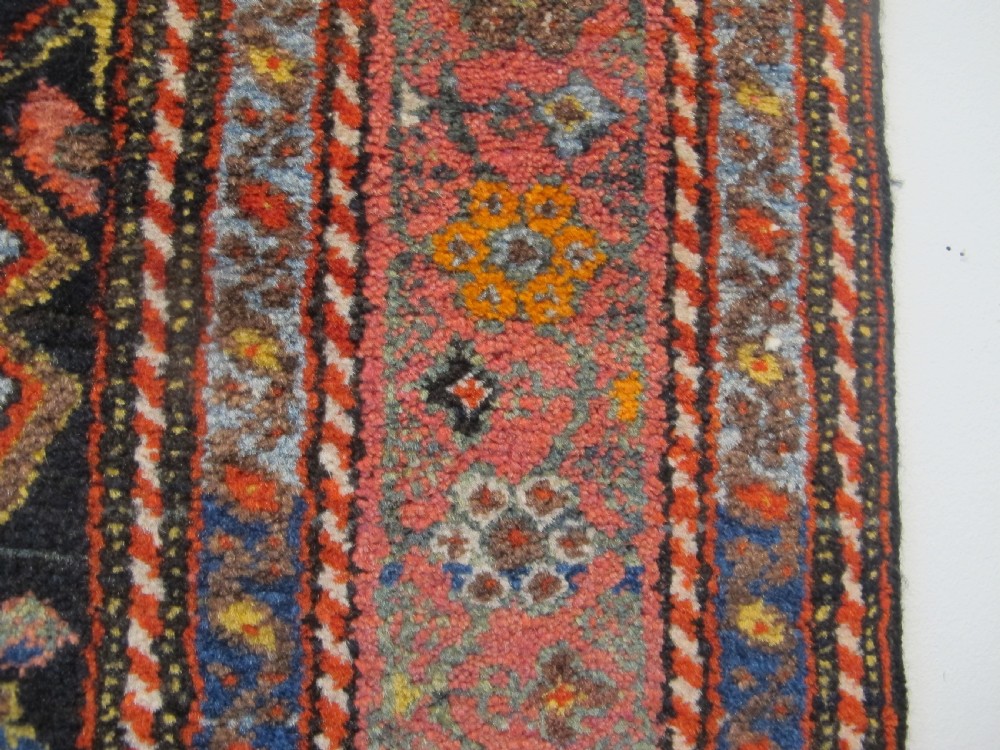 An antique hand-knotted Persian Melayir wool rug featuring an ivory central field with repeating geometric floral motifs, dark spandrels, and a terracotta border. View VI