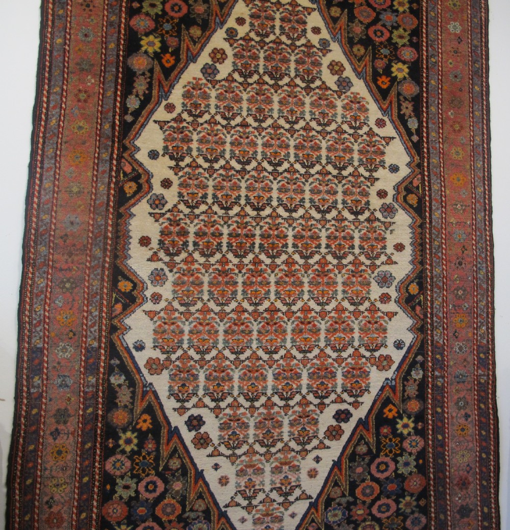 An antique hand-knotted Persian Melayir wool rug featuring an ivory central field with repeating geometric floral motifs, dark spandrels, and a terracotta border. View VIII