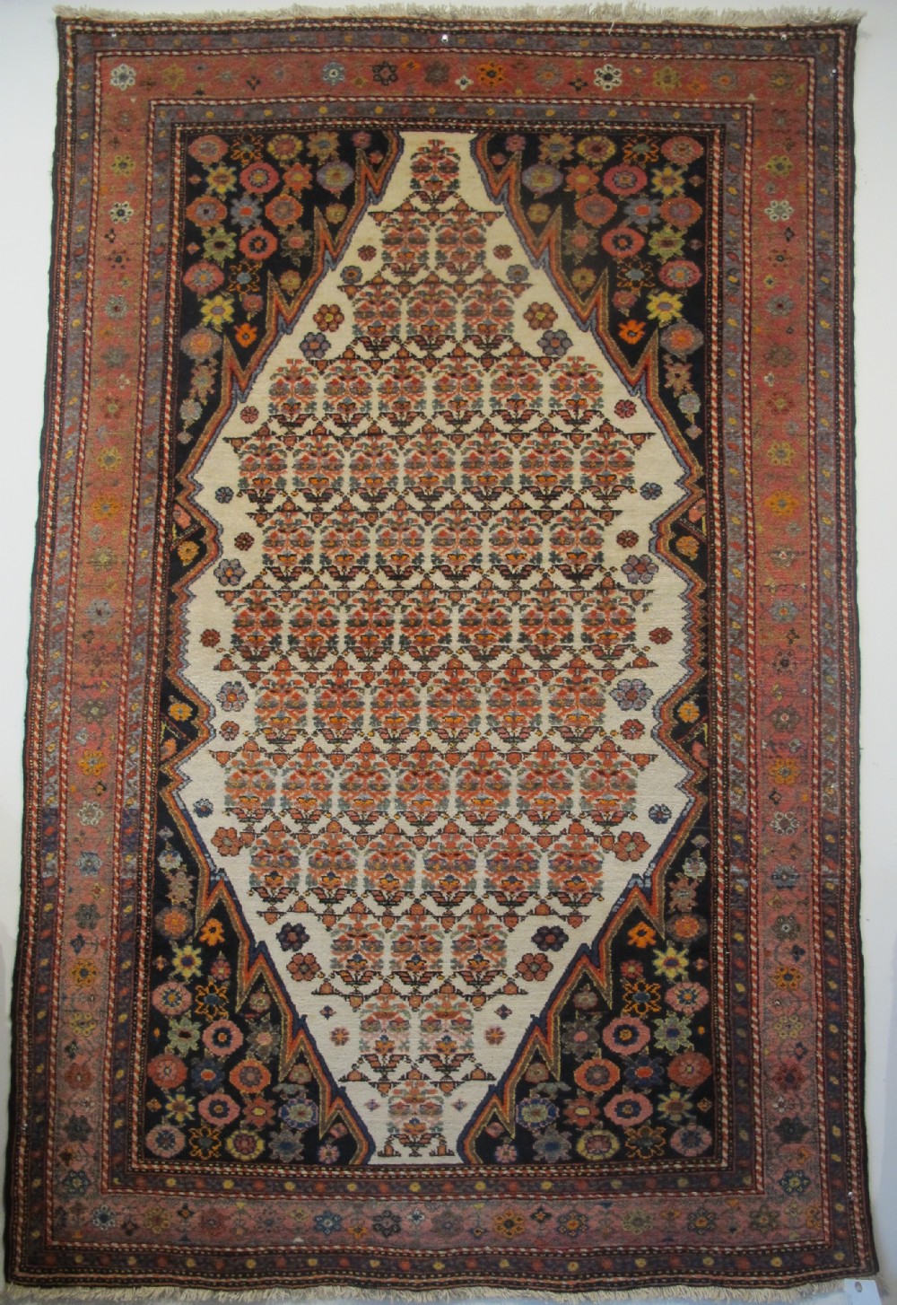 An antique hand-knotted Persian Melayir wool rug featuring an ivory central field with repeating geometric floral motifs, dark spandrels, and a terracotta border. View IX