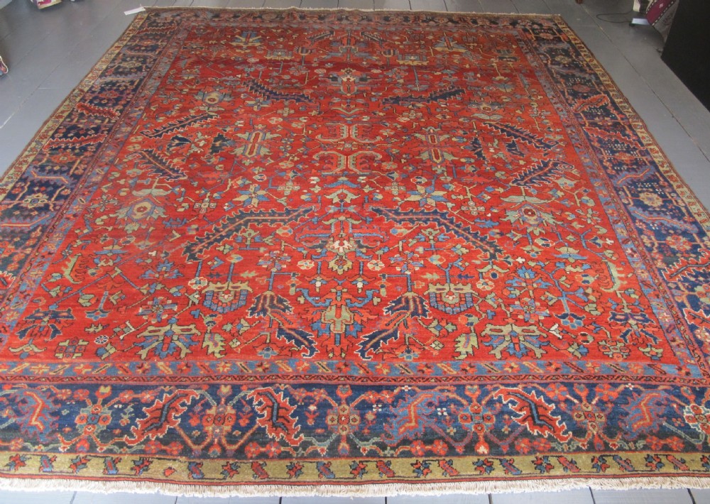 A large antique hand-knotted Persian Karaja wool carpet featuring a dominant red field with complex geometric floral medallions and a wide navy blue border.