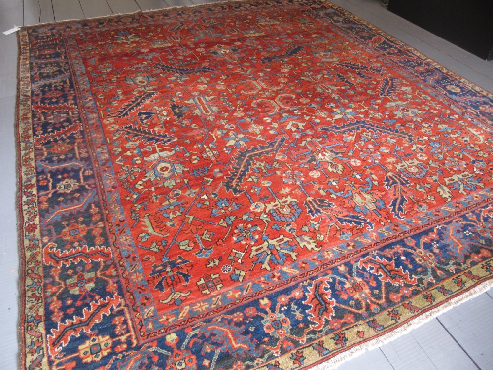 A large antique hand-knotted Persian Karaja wool carpet featuring a dominant red field with complex geometric floral medallions and a wide navy blue border. View II