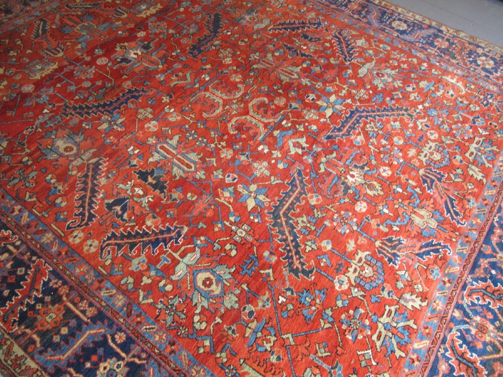 A large antique hand-knotted Persian Karaja wool carpet featuring a dominant red field with complex geometric floral medallions and a wide navy blue border. View III