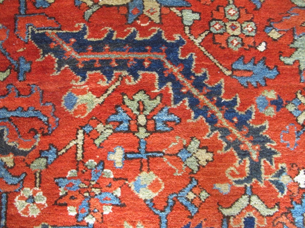 A large antique hand-knotted Persian Karaja wool carpet featuring a dominant red field with complex geometric floral medallions and a wide navy blue border. View VIII