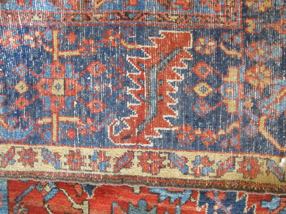 A large antique hand-knotted Persian Karaja wool carpet featuring a dominant red field with complex geometric floral medallions and a wide navy blue border. View XII