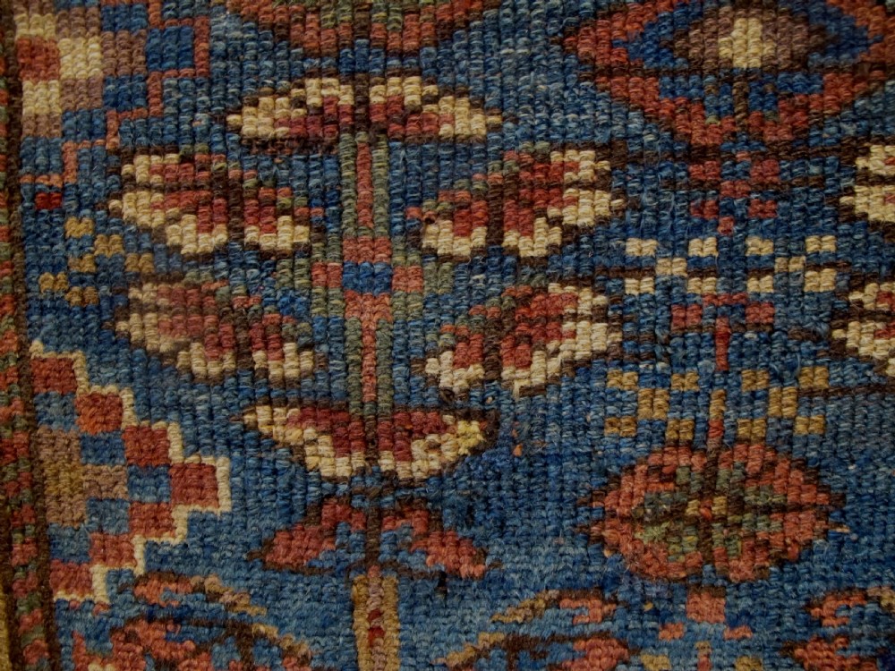 A large antique hand-knotted Persian Karaja wool carpet featuring a dominant red field with complex geometric floral medallions and a wide navy blue border. View XIII