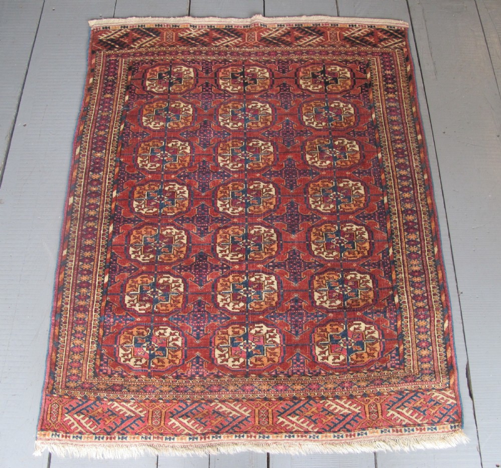 An antique woven Tekke rug featuring a deep red ground filled with grid-arranged octagonal gul motifs and geometric borders.