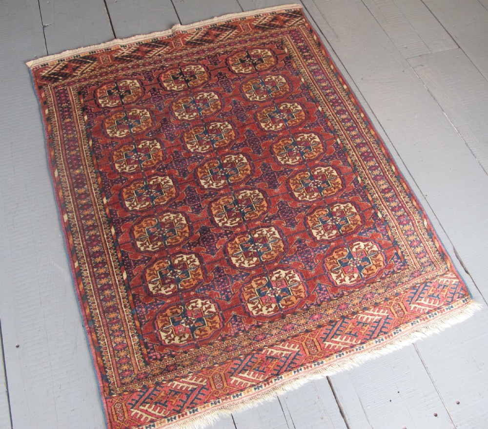 An antique woven Tekke rug featuring a deep red ground filled with grid-arranged octagonal gul motifs and geometric borders. View II