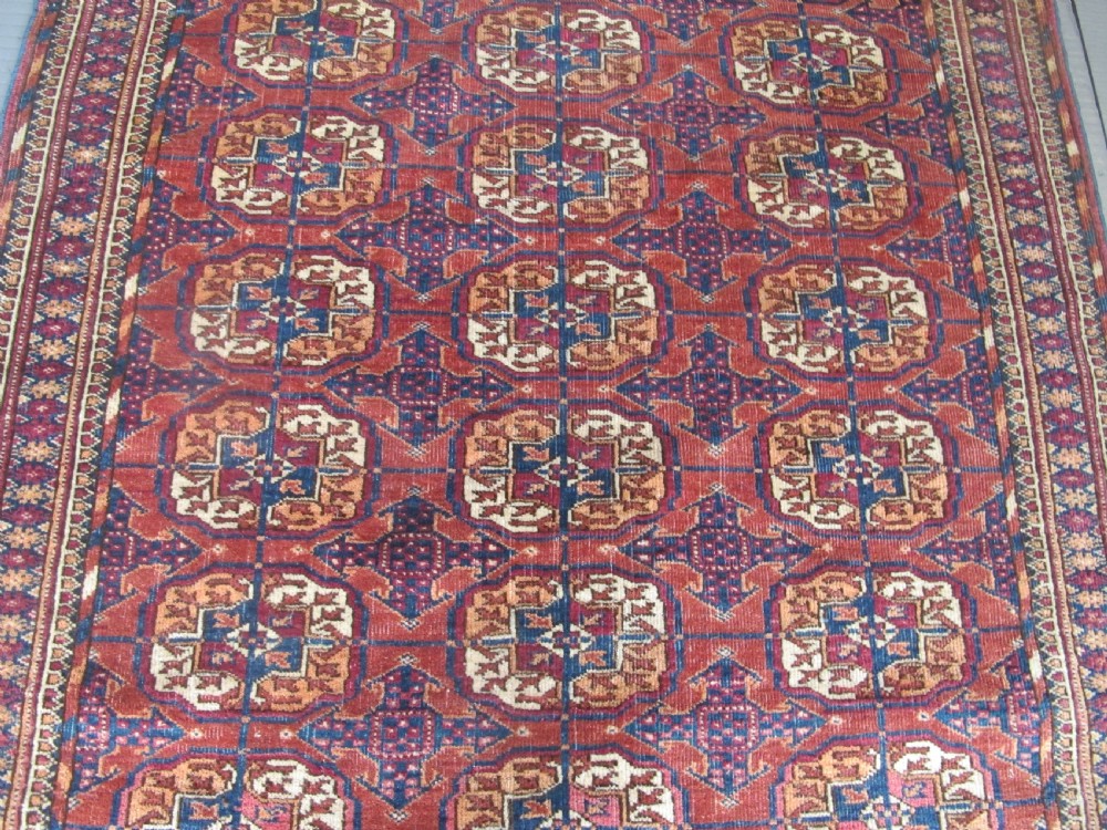 An antique woven Tekke rug featuring a deep red ground filled with grid-arranged octagonal gul motifs and geometric borders. View IV