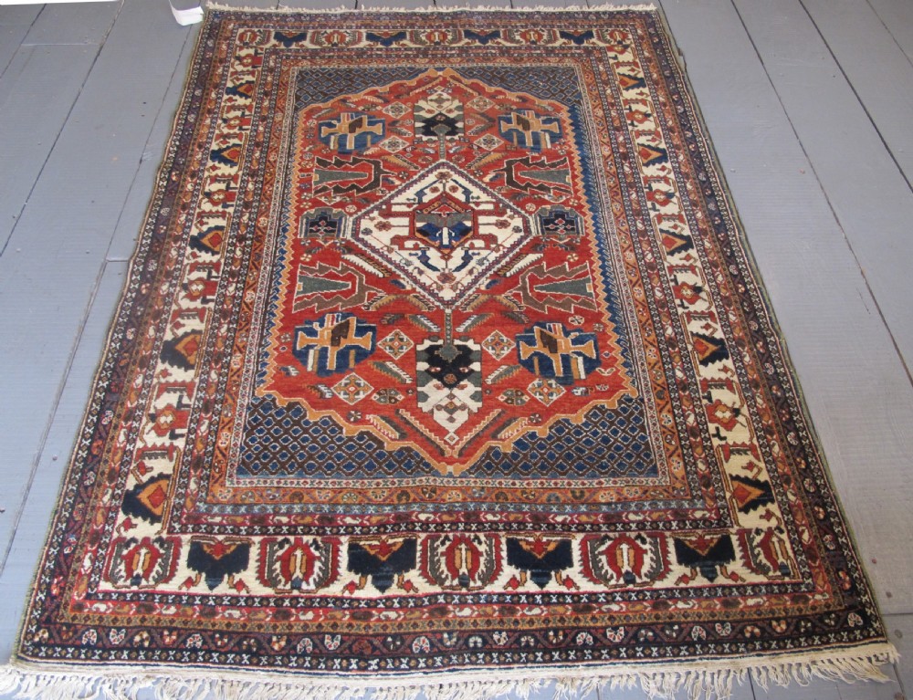 An antique South Persian hand-knotted wool rug featuring a central ivory diamond medallion within a terracotta field, bordered by indigo corners and intricate geometric bands. View II