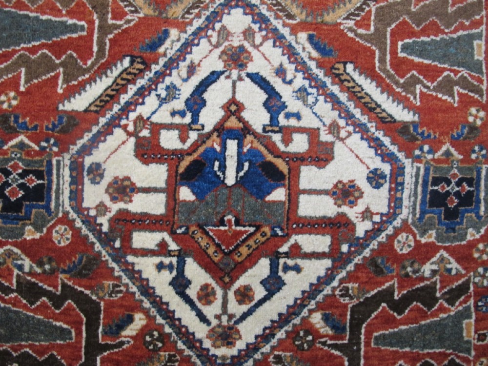 An antique South Persian hand-knotted wool rug featuring a central ivory diamond medallion within a terracotta field, bordered by indigo corners and intricate geometric bands. View III