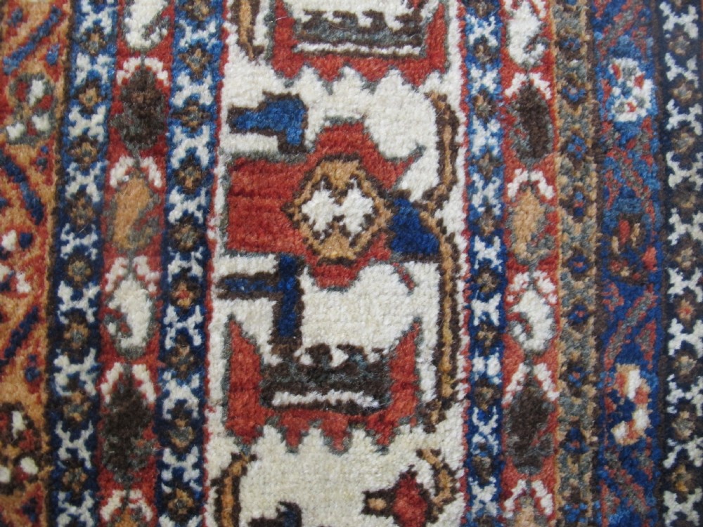 An antique South Persian hand-knotted wool rug featuring a central ivory diamond medallion within a terracotta field, bordered by indigo corners and intricate geometric bands. View IV