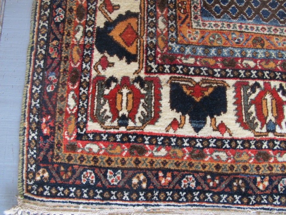 An antique South Persian hand-knotted wool rug featuring a central ivory diamond medallion within a terracotta field, bordered by indigo corners and intricate geometric bands. View V