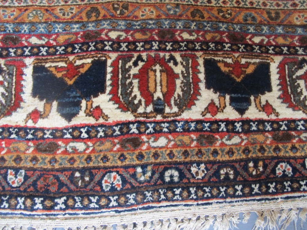 An antique South Persian hand-knotted wool rug featuring a central ivory diamond medallion within a terracotta field, bordered by indigo corners and intricate geometric bands. View VI