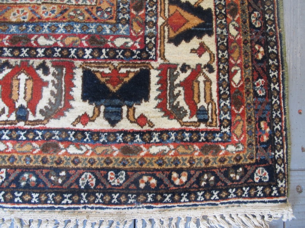 An antique South Persian hand-knotted wool rug featuring a central ivory diamond medallion within a terracotta field, bordered by indigo corners and intricate geometric bands. View VII