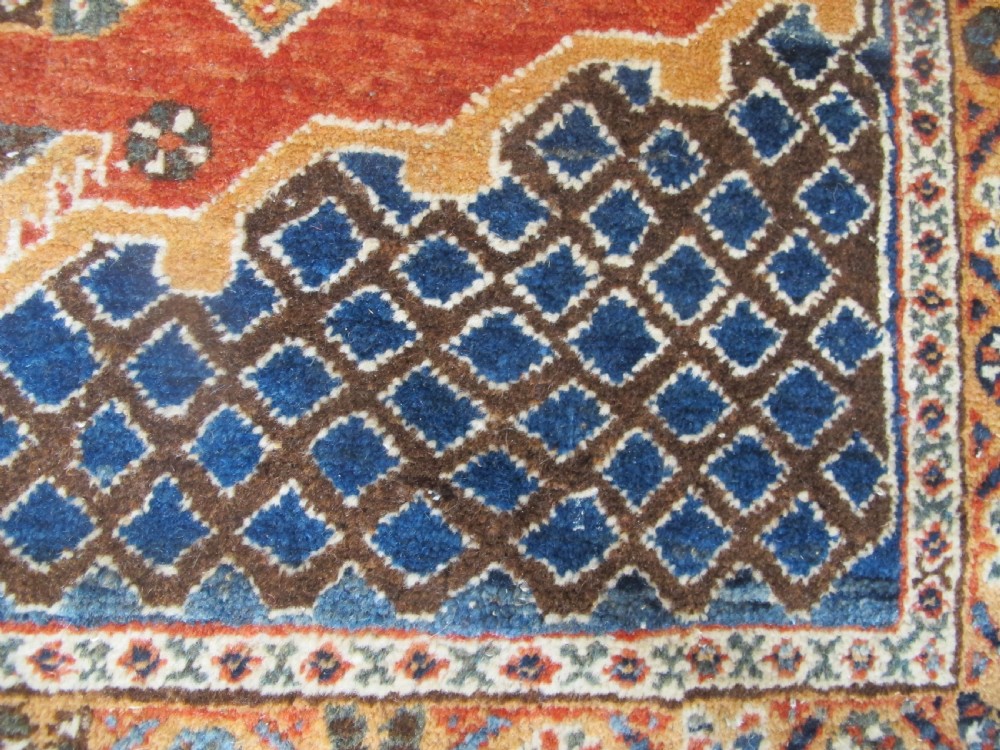 An antique South Persian hand-knotted wool rug featuring a central ivory diamond medallion within a terracotta field, bordered by indigo corners and intricate geometric bands. View VIII