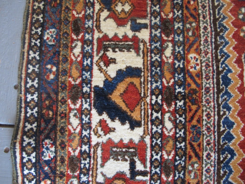 An antique South Persian hand-knotted wool rug featuring a central ivory diamond medallion within a terracotta field, bordered by indigo corners and intricate geometric bands. View X