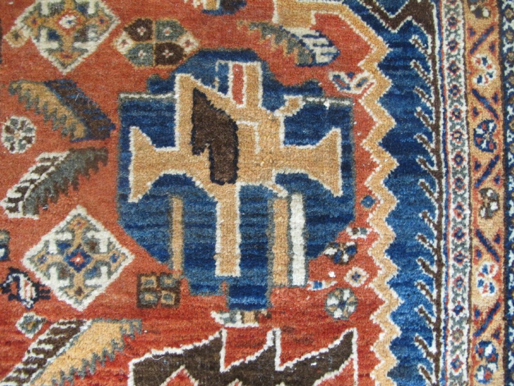 An antique South Persian hand-knotted wool rug featuring a central ivory diamond medallion within a terracotta field, bordered by indigo corners and intricate geometric bands. View XI
