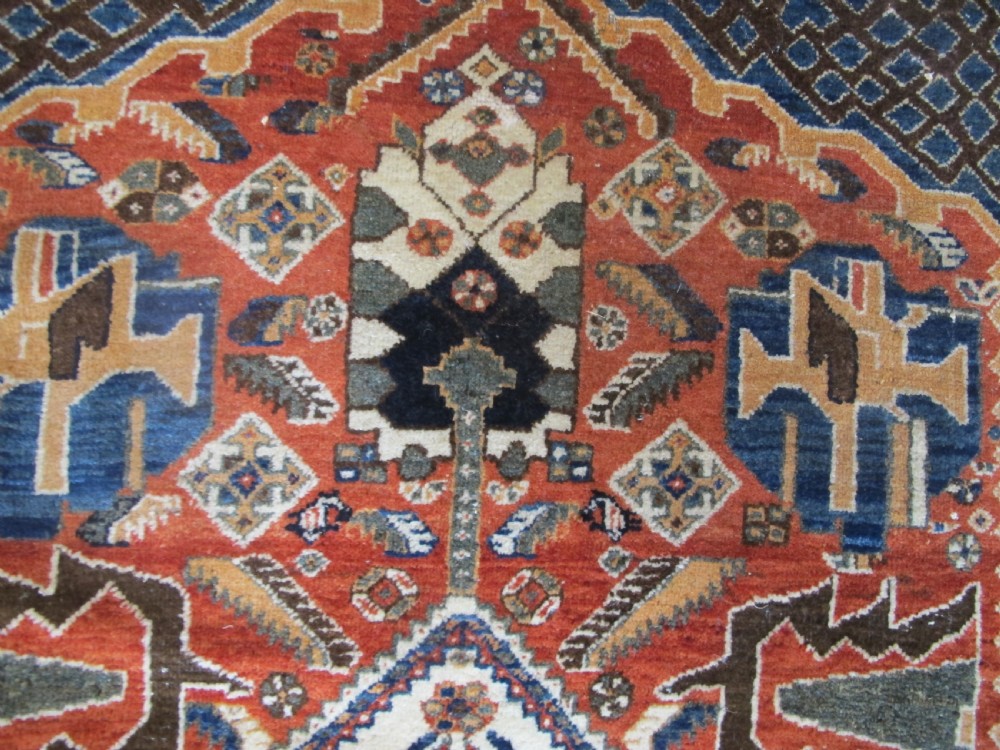 An antique South Persian hand-knotted wool rug featuring a central ivory diamond medallion within a terracotta field, bordered by indigo corners and intricate geometric bands. View XII