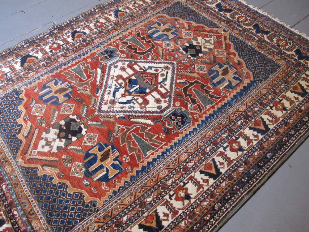 An antique South Persian hand-knotted wool rug featuring a central ivory diamond medallion within a terracotta field, bordered by indigo corners and intricate geometric bands. View XIV