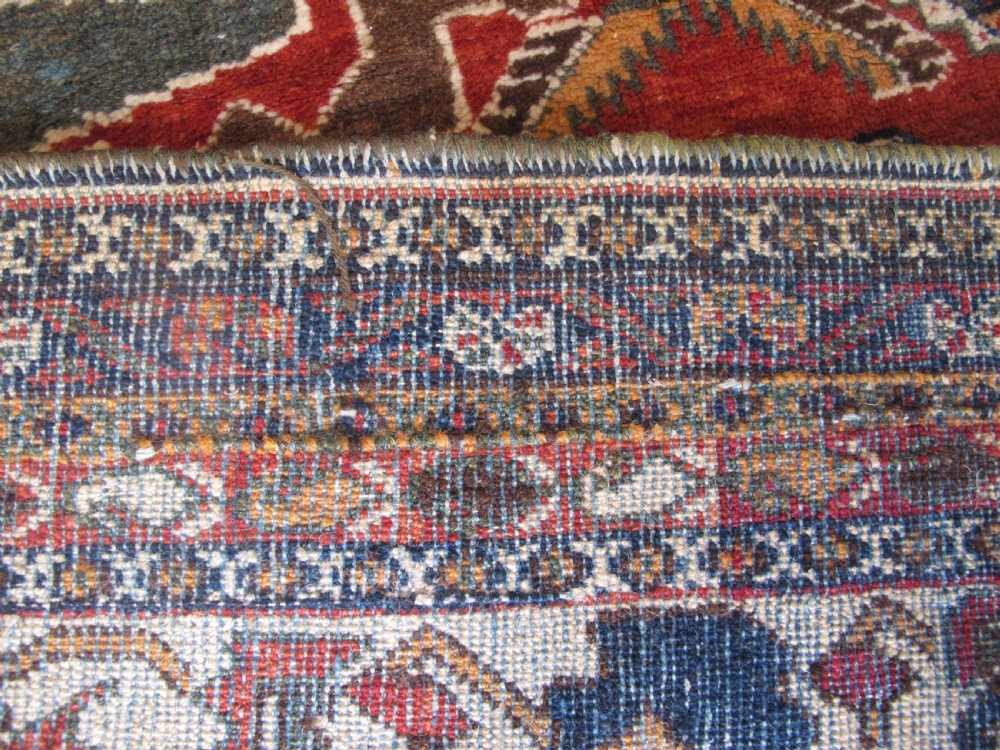 An antique South Persian hand-knotted wool rug featuring a central ivory diamond medallion within a terracotta field, bordered by indigo corners and intricate geometric bands. View XV