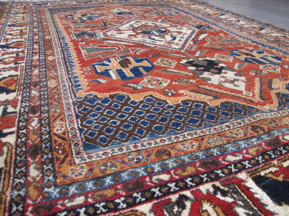 An antique South Persian hand-knotted wool rug featuring a central ivory diamond medallion within a terracotta field, bordered by indigo corners and intricate geometric bands. View XVI