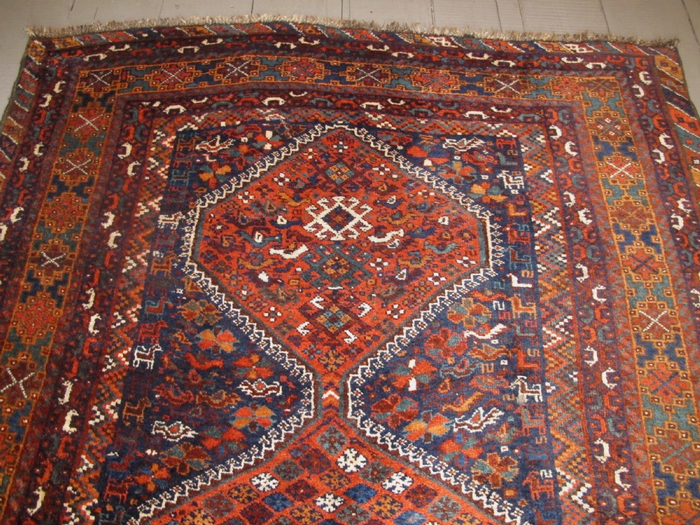 An antique hand-knotted Persian tribal rug featuring three central diamond medallions surrounded by geometric patterns in deep red, navy blue, and terracotta tones. View II