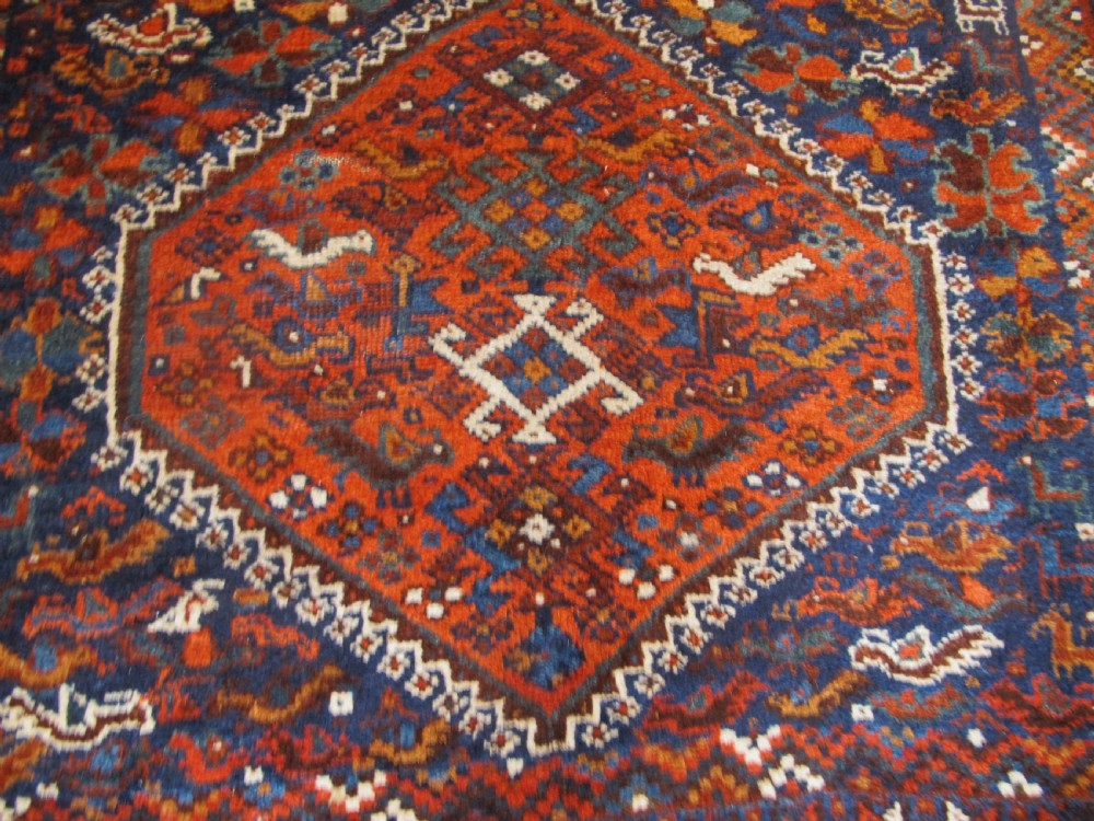An antique hand-knotted Persian tribal rug featuring three central diamond medallions surrounded by geometric patterns in deep red, navy blue, and terracotta tones. View III
