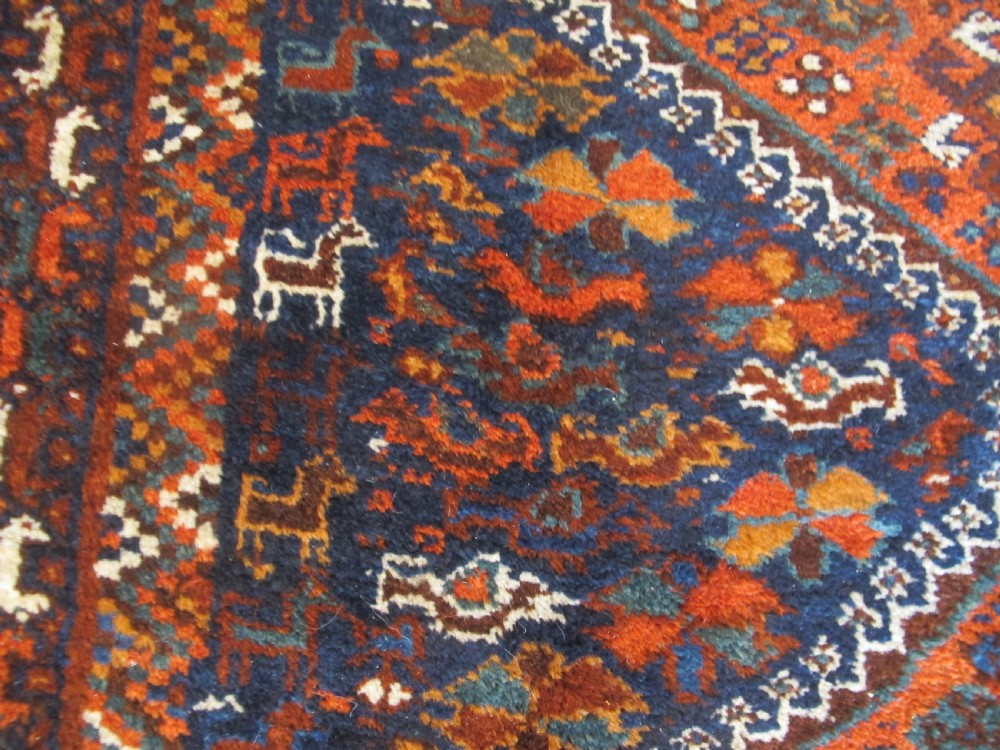 An antique hand-knotted Persian tribal rug featuring three central diamond medallions surrounded by geometric patterns in deep red, navy blue, and terracotta tones. View IV