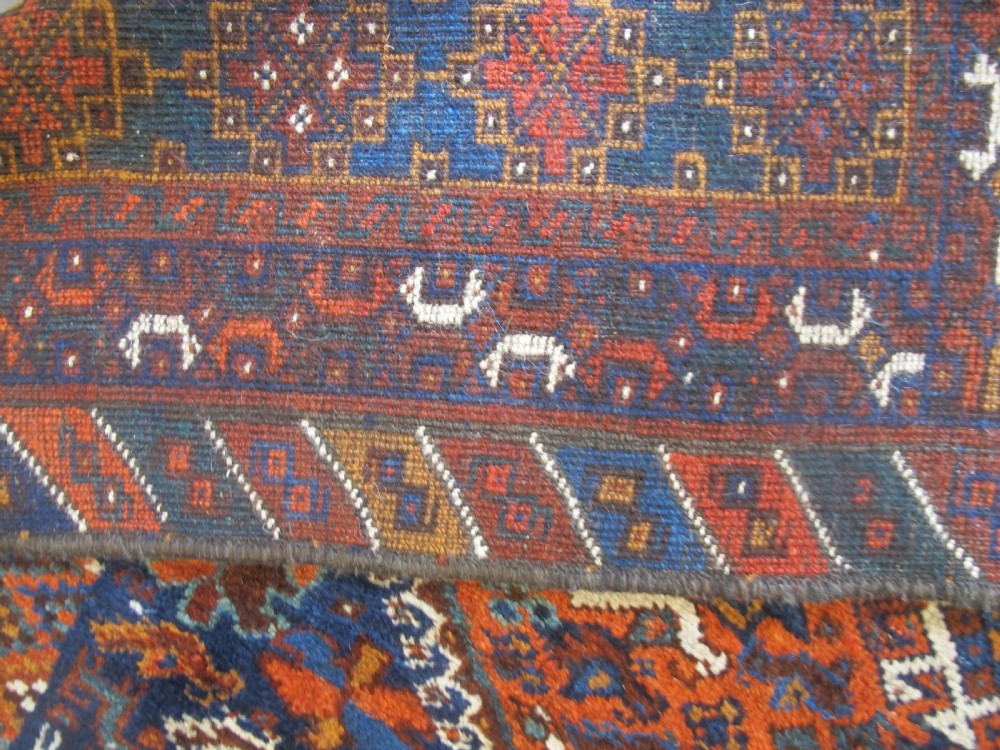 An antique hand-knotted Persian tribal rug featuring three central diamond medallions surrounded by geometric patterns in deep red, navy blue, and terracotta tones. View VII