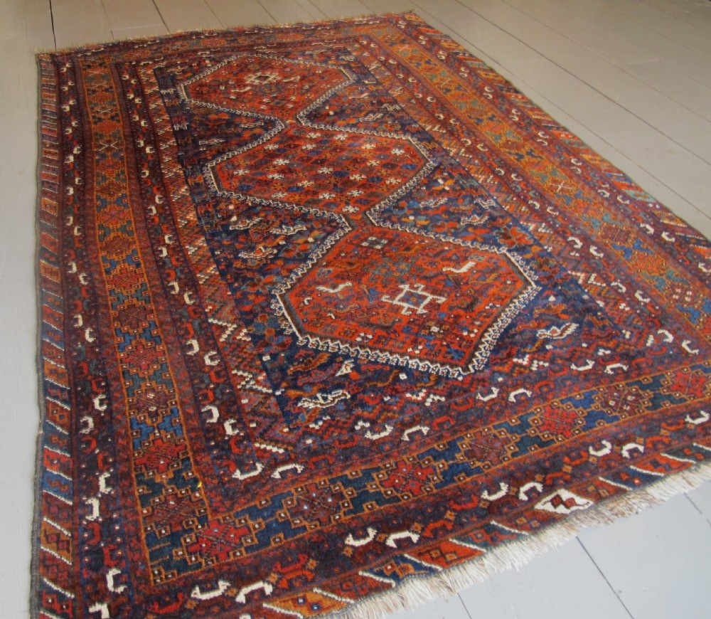 An antique hand-knotted Persian tribal rug featuring three central diamond medallions surrounded by geometric patterns in deep red, navy blue, and terracotta tones. View IX