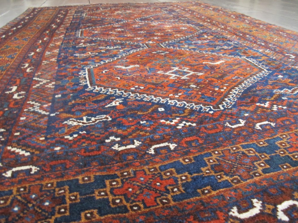 An antique hand-knotted Persian tribal rug featuring three central diamond medallions surrounded by geometric patterns in deep red, navy blue, and terracotta tones. View XI