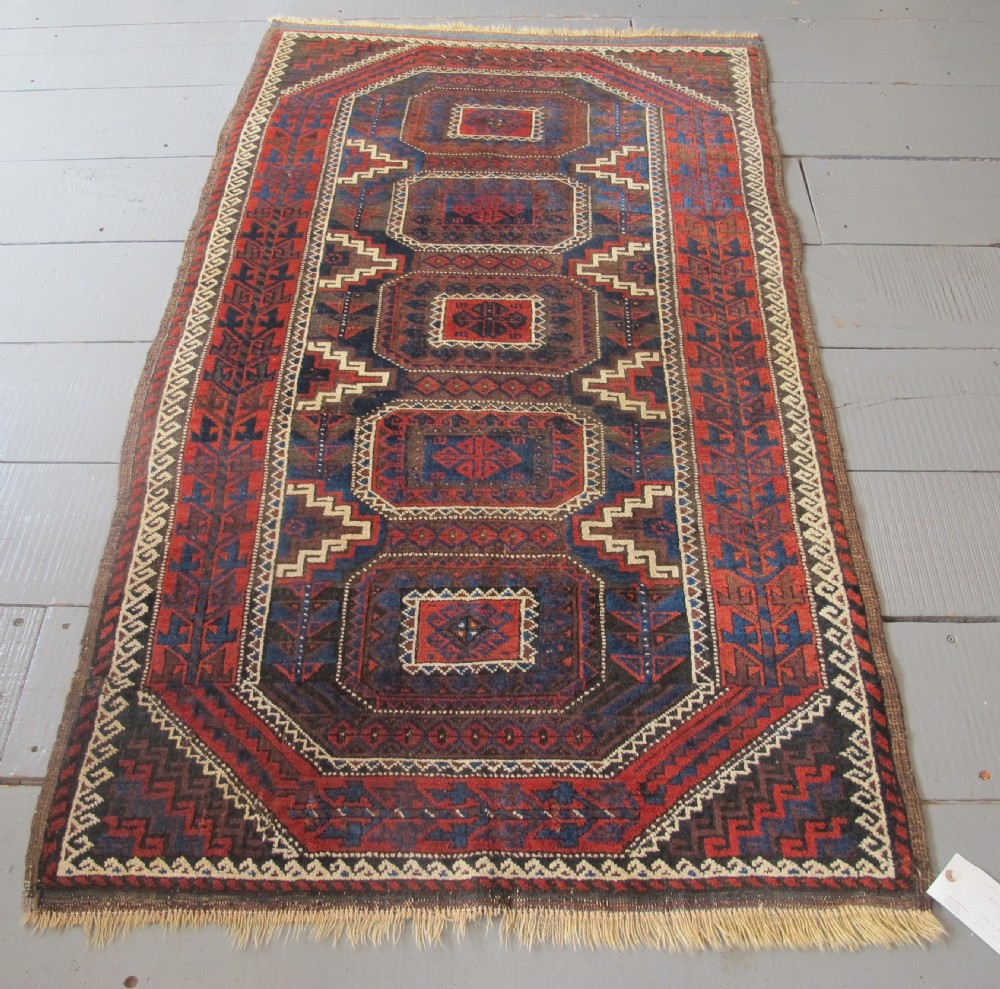 An antique hand-woven Belouch wool rug featuring geometric octagonal medallions in deep red, navy blue, and dark brown tones.