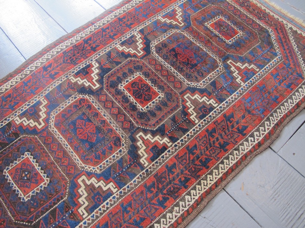 An antique hand-woven Belouch wool rug featuring geometric octagonal medallions in deep red, navy blue, and dark brown tones. View II