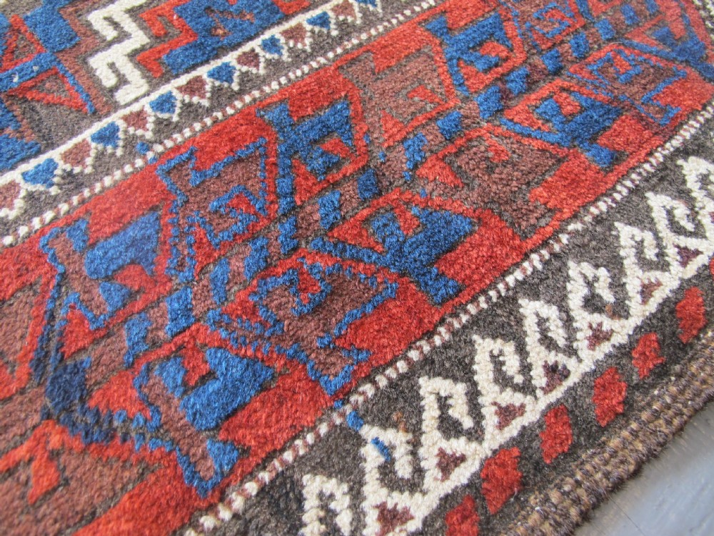 An antique hand-woven Belouch wool rug featuring geometric octagonal medallions in deep red, navy blue, and dark brown tones. View III