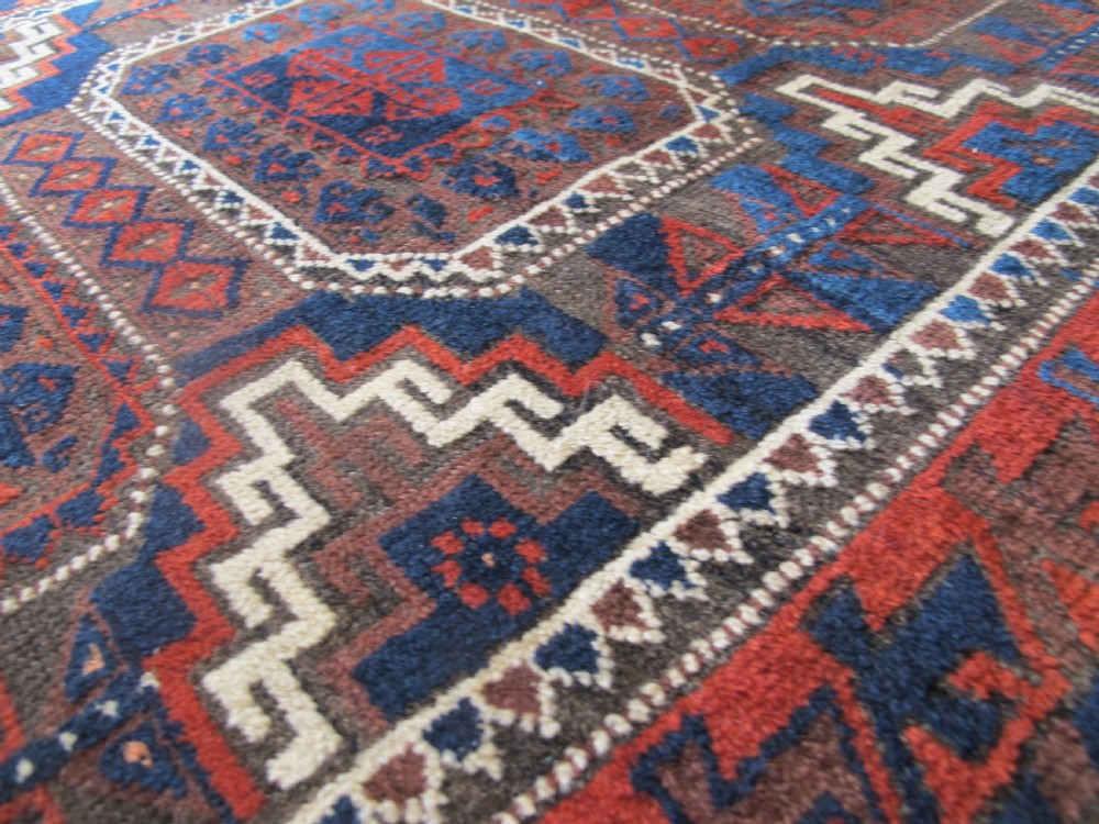 An antique hand-woven Belouch wool rug featuring geometric octagonal medallions in deep red, navy blue, and dark brown tones. View IV